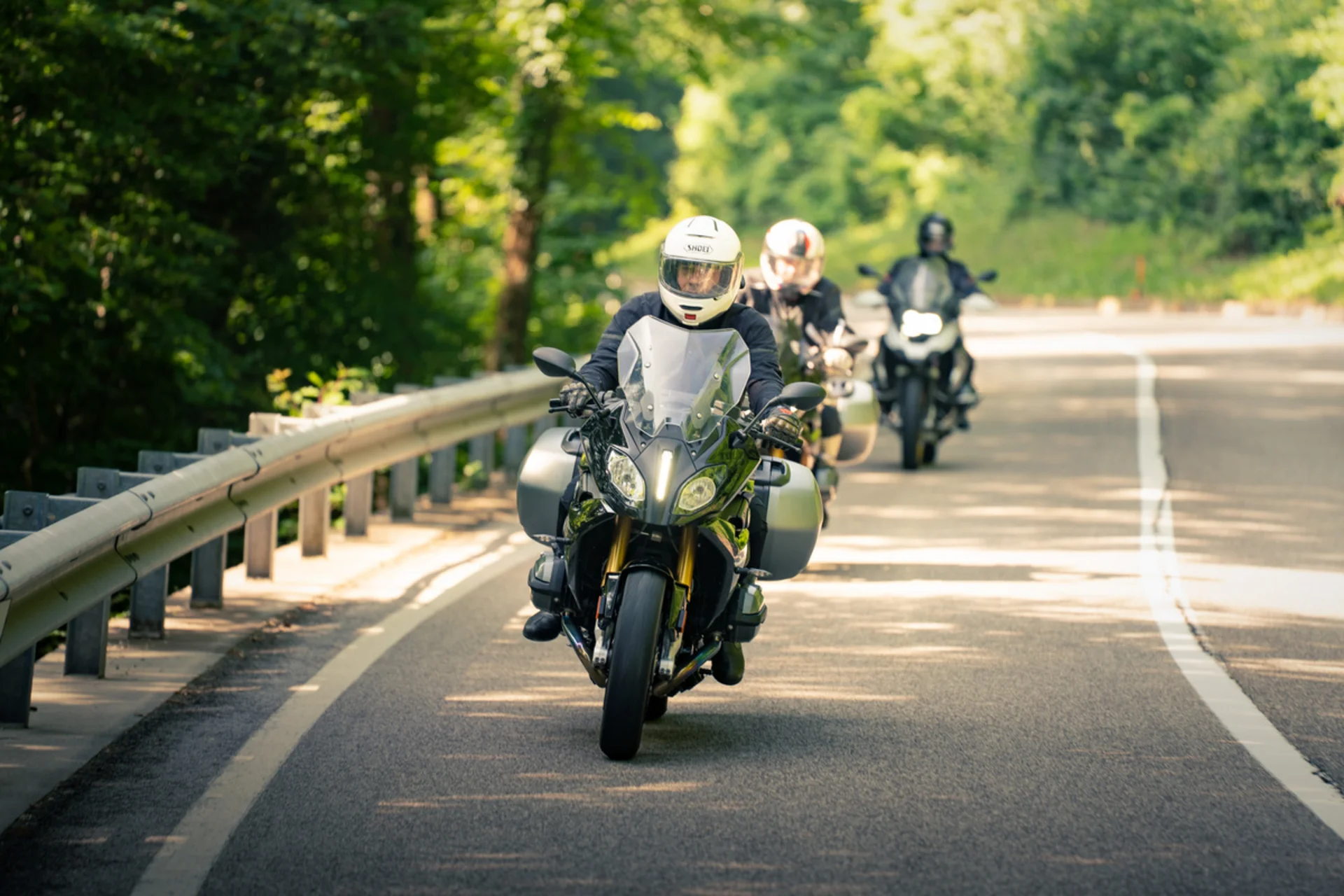 Three motorcyclists riding on a winding road through the forest