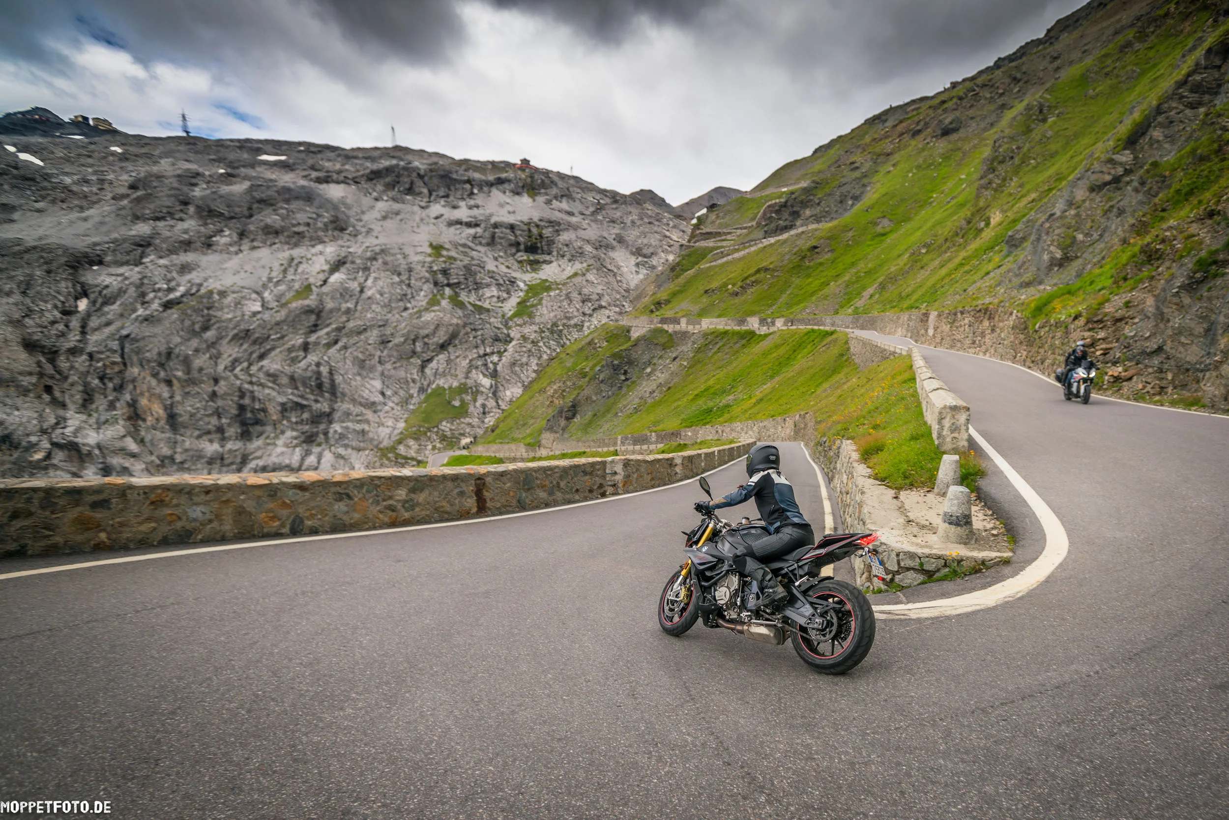 Motorrad-Touren © Moppetfoto.de Motorradfahrer auf kurviger Bergstraße mit steilen Felswänden und Wolken
