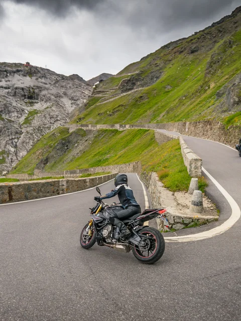 Motorcyclists riding on winding mountain road with rocky cliffs and cloudy sky