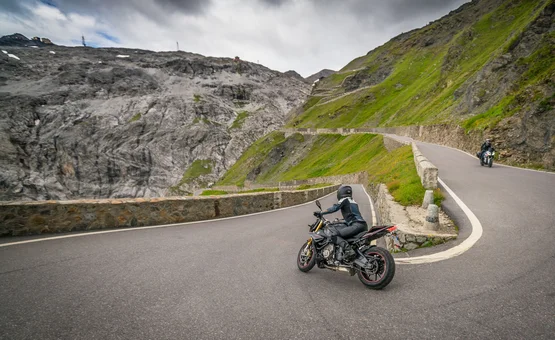 Motorcyclists riding on winding mountain road with rocky cliffs and cloudy sky
