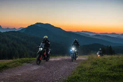 Drie motorfietsers op een bergpad bij zonsondergang