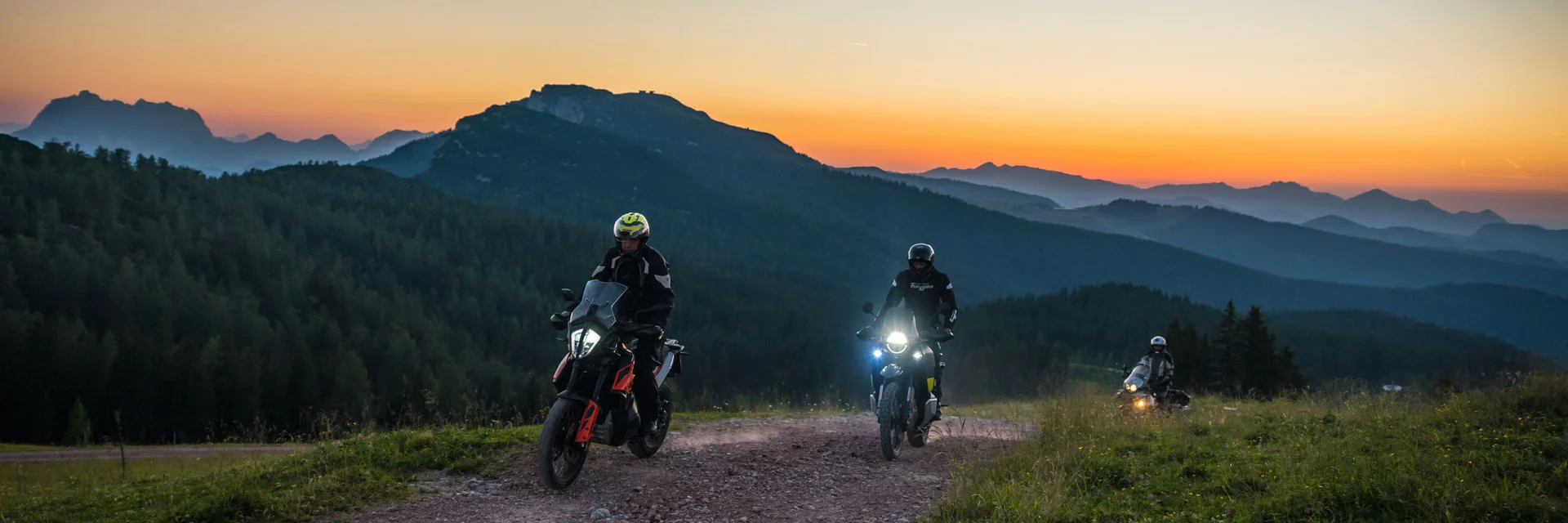 Drie motorfietsers op een bergpad bij zonsondergang