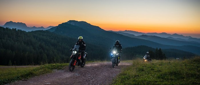 Drei Motorradfahrer fahren auf einem Bergweg bei Sonnenuntergang