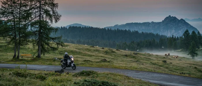 Motorcyclist riding on a mountain road in fog at sunset