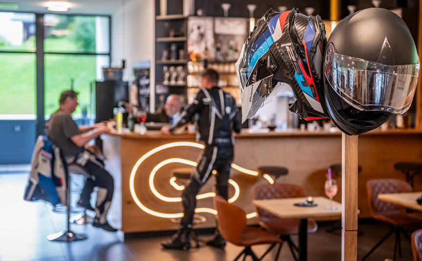 Motorradhelme an einem Ständer in einem Café mit Personen im Hintergrund