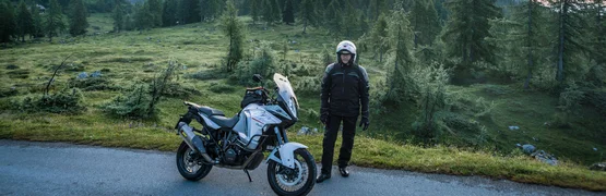 Motorrijder met helm naast motor in berglandschap bij zonsopgang