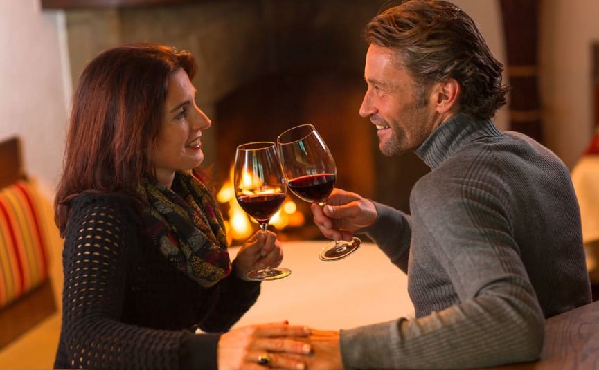 Paar trinkt gemeinsam Rotwein am Kamin und hält Händchen