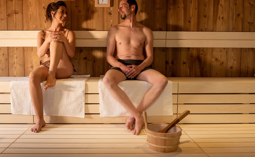 Mann und Frau entspannen in der Sauna auf Holzbänken mit Saunakübel davor