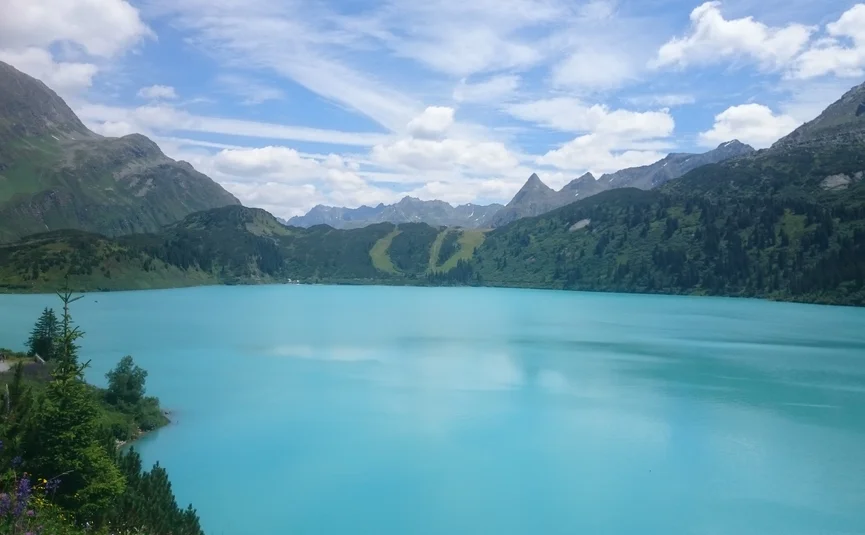 Blue mountain lake surrounded by green hills under a blue sky with clouds