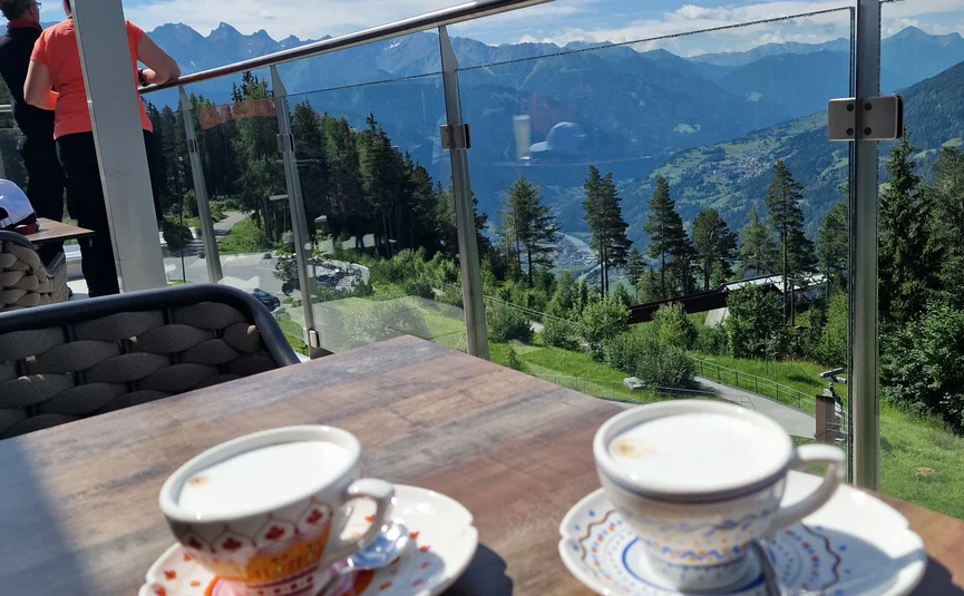 Twee koffiekoppen op tafel met uitzicht op bergen en blauwe lucht