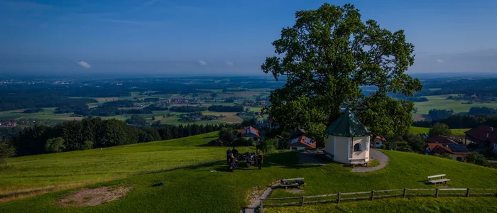 Kapelle unter großem Baum auf Hügel mit weitem Talblick