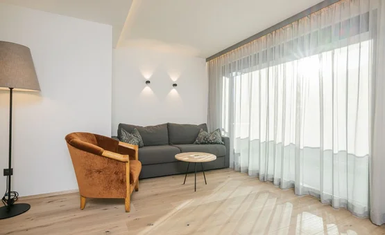 Golden Summit Days Moderner Wohnbereich mit brauem Sessel, grauem Sofa und Vorhängen an großen Fenstern