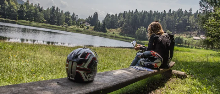 Val di Fiemme © A. Monticelli Frau mit Motorradhelm am See mit Wald und Bergen im Hintergrund