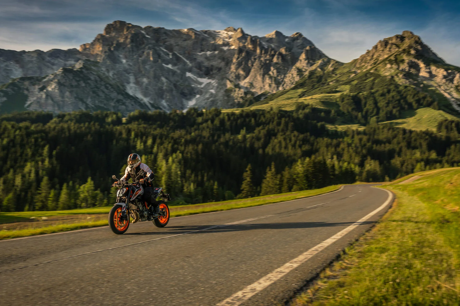 Motorradfahrer auf Bergstraße mit bewaldeten Hügeln und steilen Gipfeln im Hintergrund