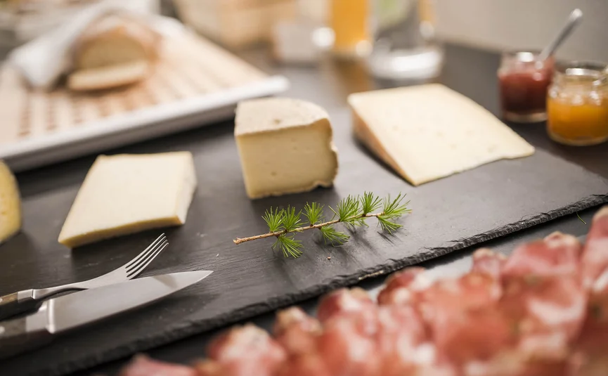 Verschillende kazen en vleeswaren op een zwart serveerbord met kruiden takje