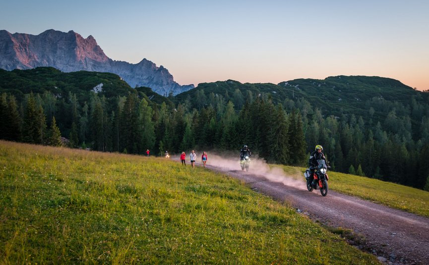 Motorradfahrer und Wanderer auf einem Waldweg mit Bergen im Hintergrund