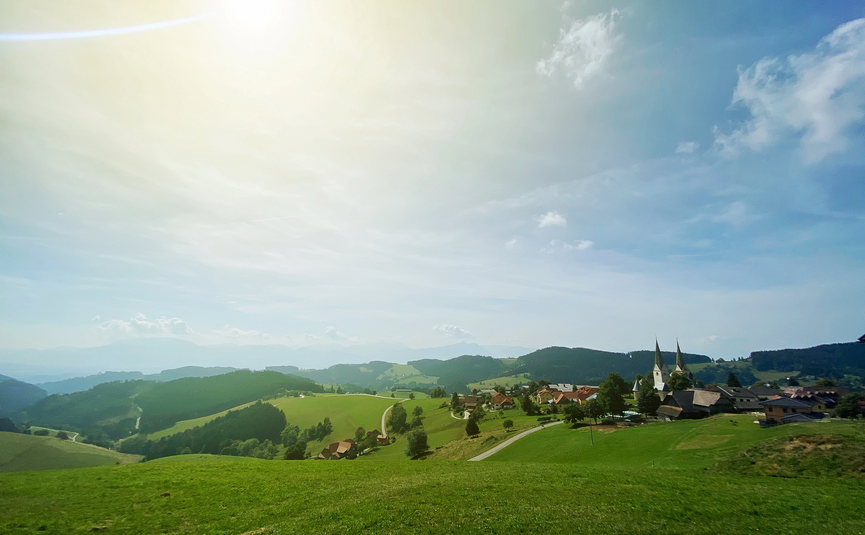 Sonniger Tag über grünen Hügeln und einem Dorf mit Kirchtürmen