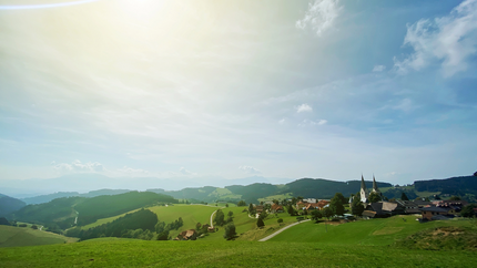 Sonniger Tag über grünen Hügeln und einem Dorf mit Kirchtürmen