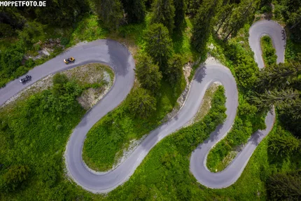 Luchtfoto van een kronkelende bergweg met motorfietsen en groene begroeiing