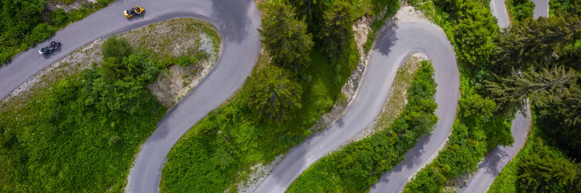 Luftaufnahme einer kurvigen Bergstraße mit Motorrädern und grüner Vegetation