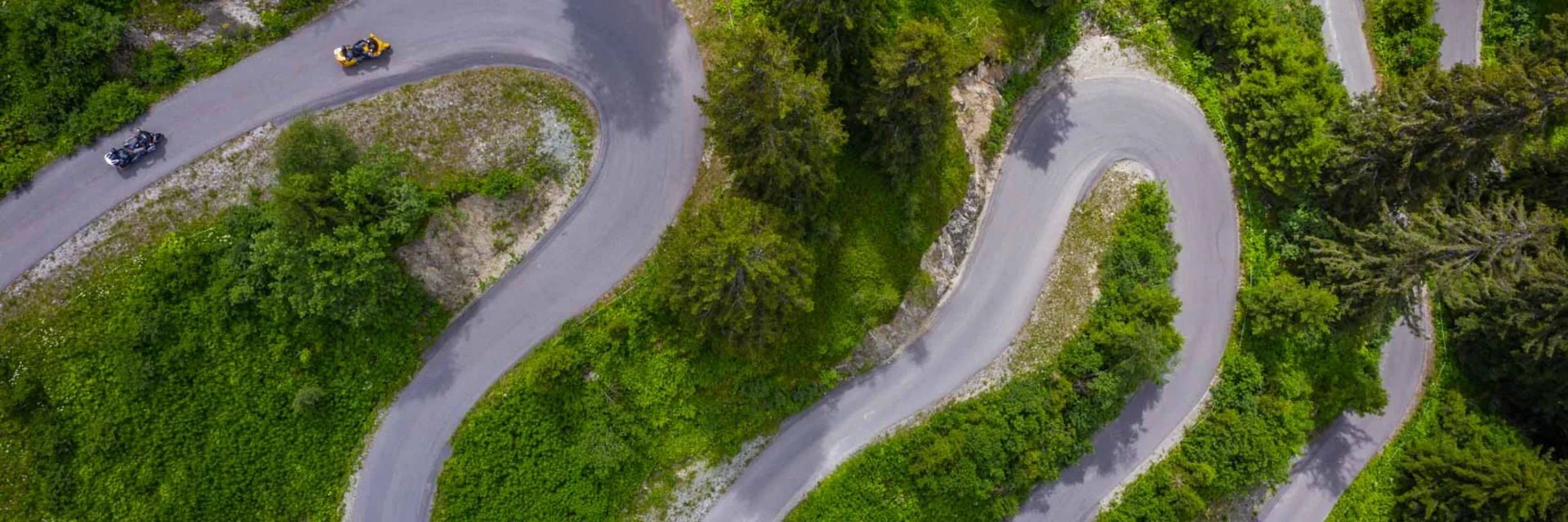 Luftaufnahme einer kurvigen Bergstraße mit Motorrädern und grüner Vegetation