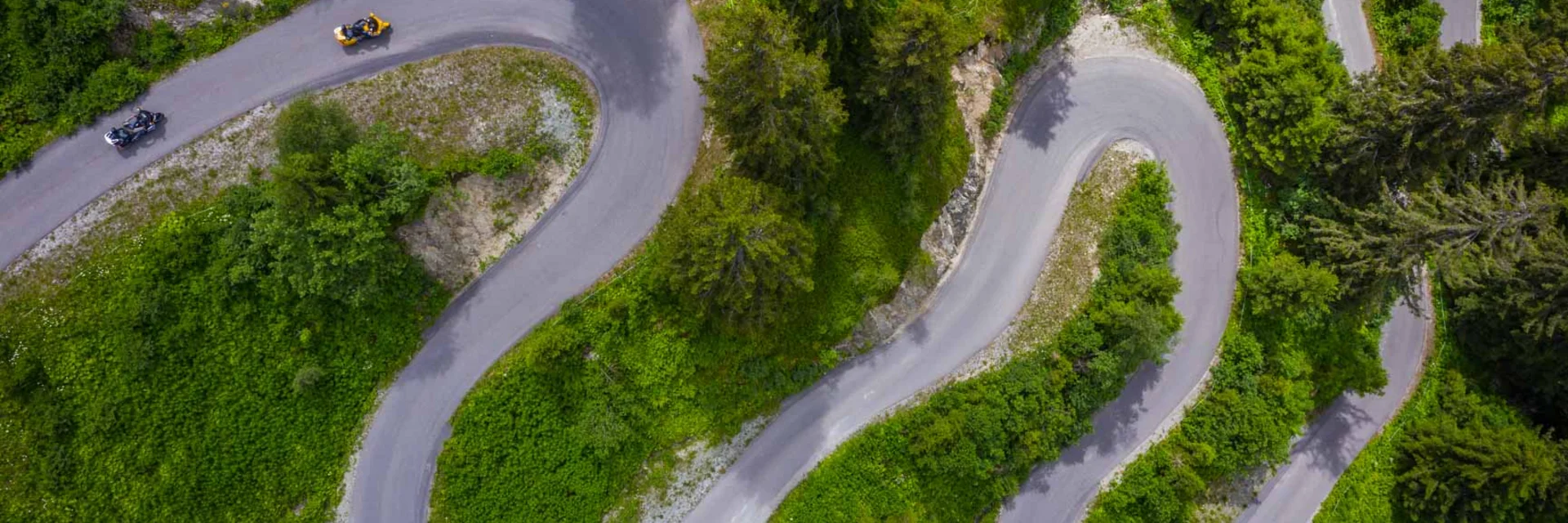 Aerial view of a winding mountain road with motorcycles and green vegetation