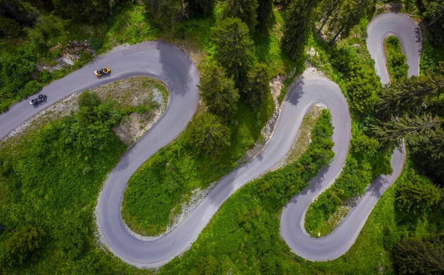 Motorbike holiday in Tyrol © Moppetfoto.de Aerial view of a winding mountain road with motorcycles and green vegetation