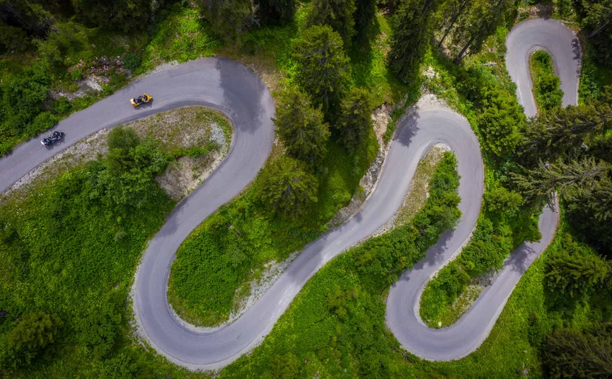 Motorradurlaub in Tirol © Moppetfoto.de Luftaufnahme einer kurvigen Bergstraße mit Motorrädern und grüner Vegetation
