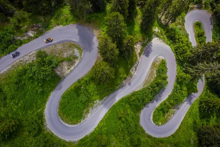Luchtfoto van een kronkelende bergweg met motorfietsen en groene begroeiing