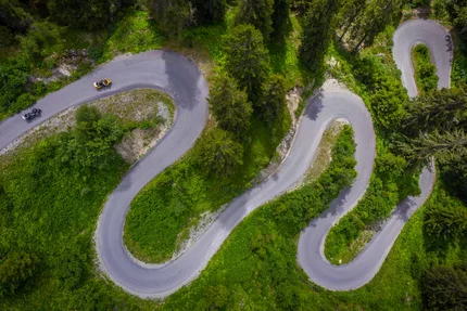 Aerial view of a winding mountain road with motorcycles and green vegetation