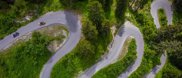 Luftaufnahme einer kurvigen Bergstraße mit Motorrädern und grüner Vegetation