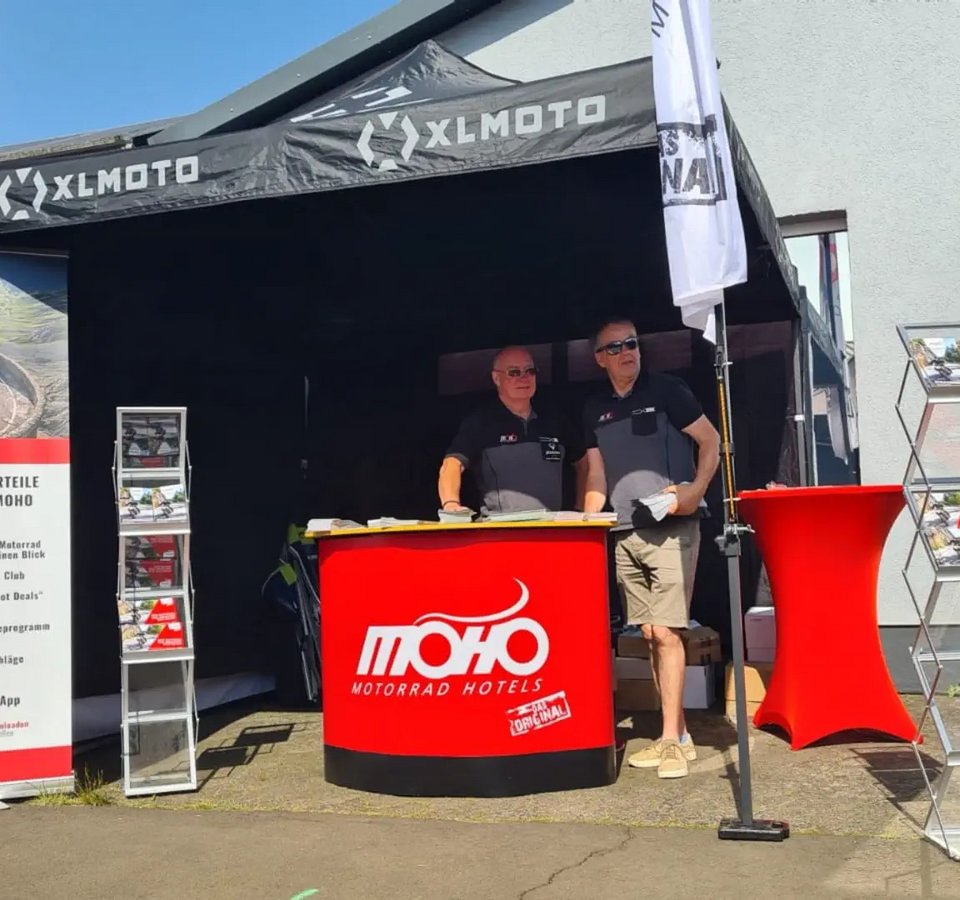 Messestand von MoHo Motorrad Hotels mit zwei Männern und Informationsmaterial