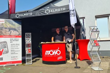 Messestand von MoHo Motorrad Hotels mit zwei Männern und Informationsmaterial