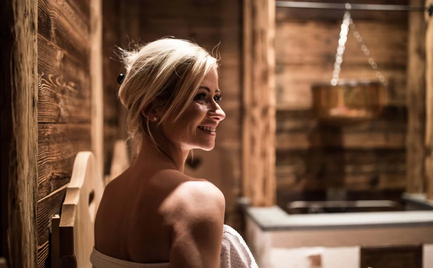 Woman in towel sitting in wooden sauna with warm lighting