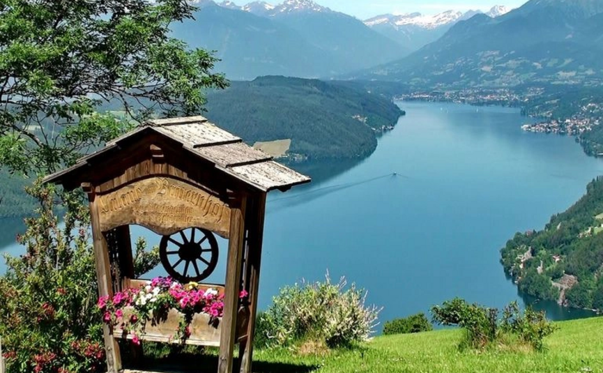 Holzbrunnen mit Blumen vor Bergsee und schneebedeckten Bergen