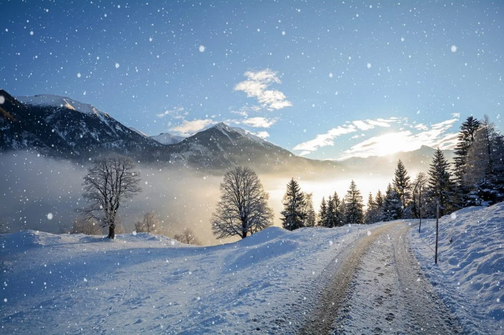 Verschneite Berglandschaft mit Wald, verschneitem Weg und fallenden Schneeflocken