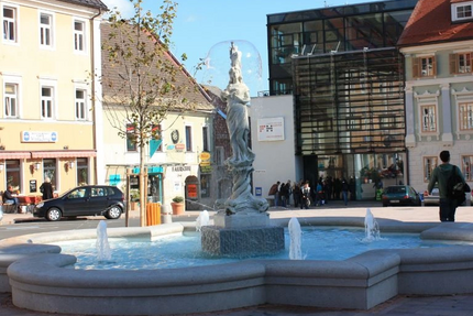 Brunnen mit Statue in einem belebten Stadtplatz bei Sonnenschein