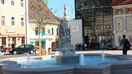 Brunnen mit Statue in einem belebten Stadtplatz bei Sonnenschein