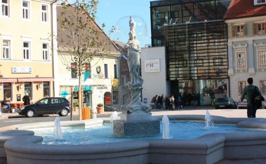 Kärntner-Seenrunde Brunnen mit Statue in einem belebten Stadtplatz bei Sonnenschein
