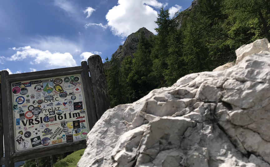 Steinschild mit Aufschrift Vršič 1611m in Berglandschaft mit Bäumen und Wolken