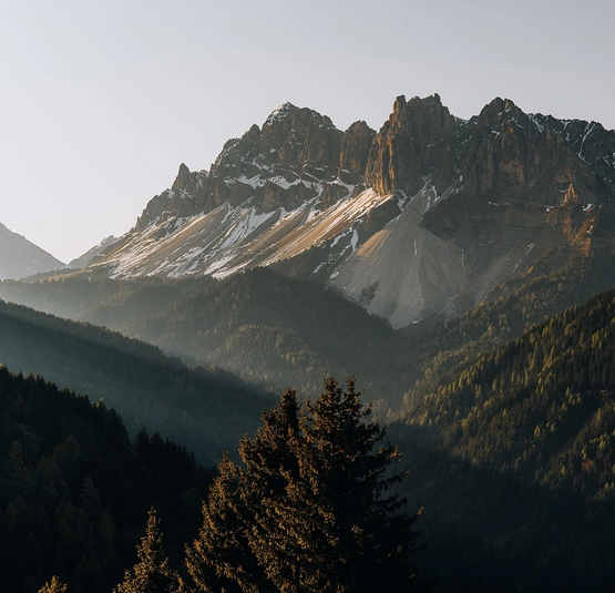 Bergpanorama mit bewaldeten Hügeln und schneebedeckten Gipfeln im Morgenlicht