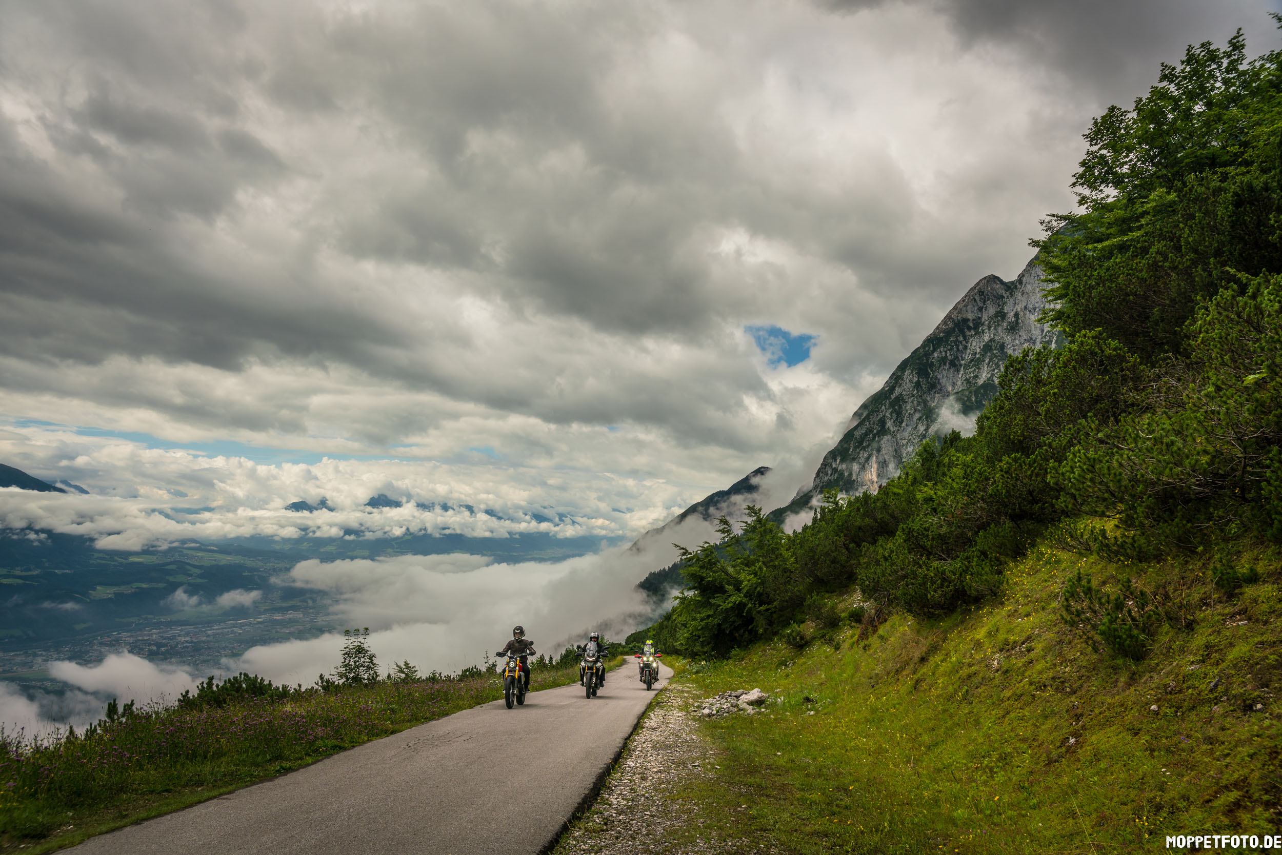 Drei Motorräder fahren auf einer Bergstraße mit Wolken und grüner Landschaft