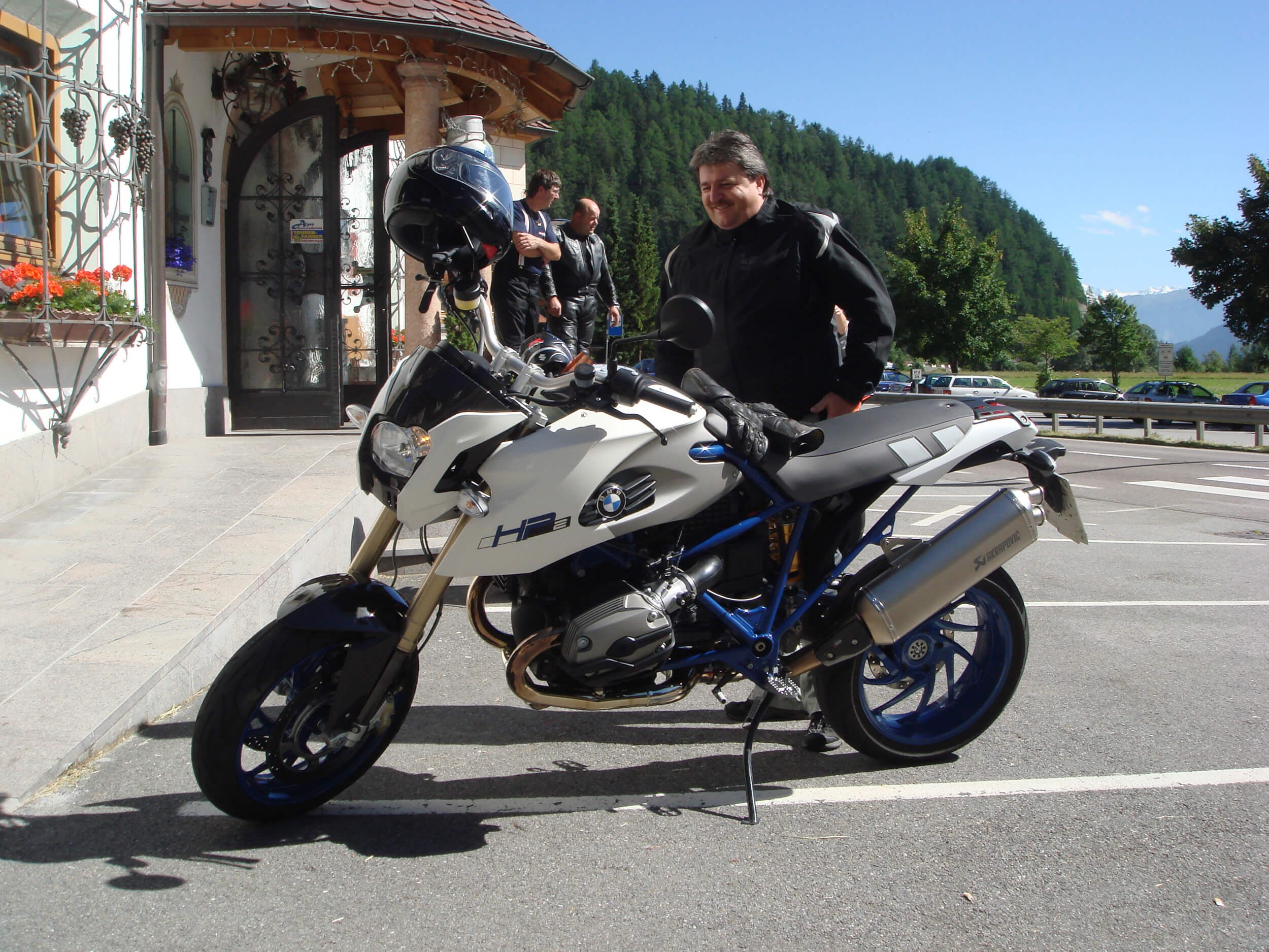 Man standing next to white and blue BMW HP2 motorcycle in sunny mountain area