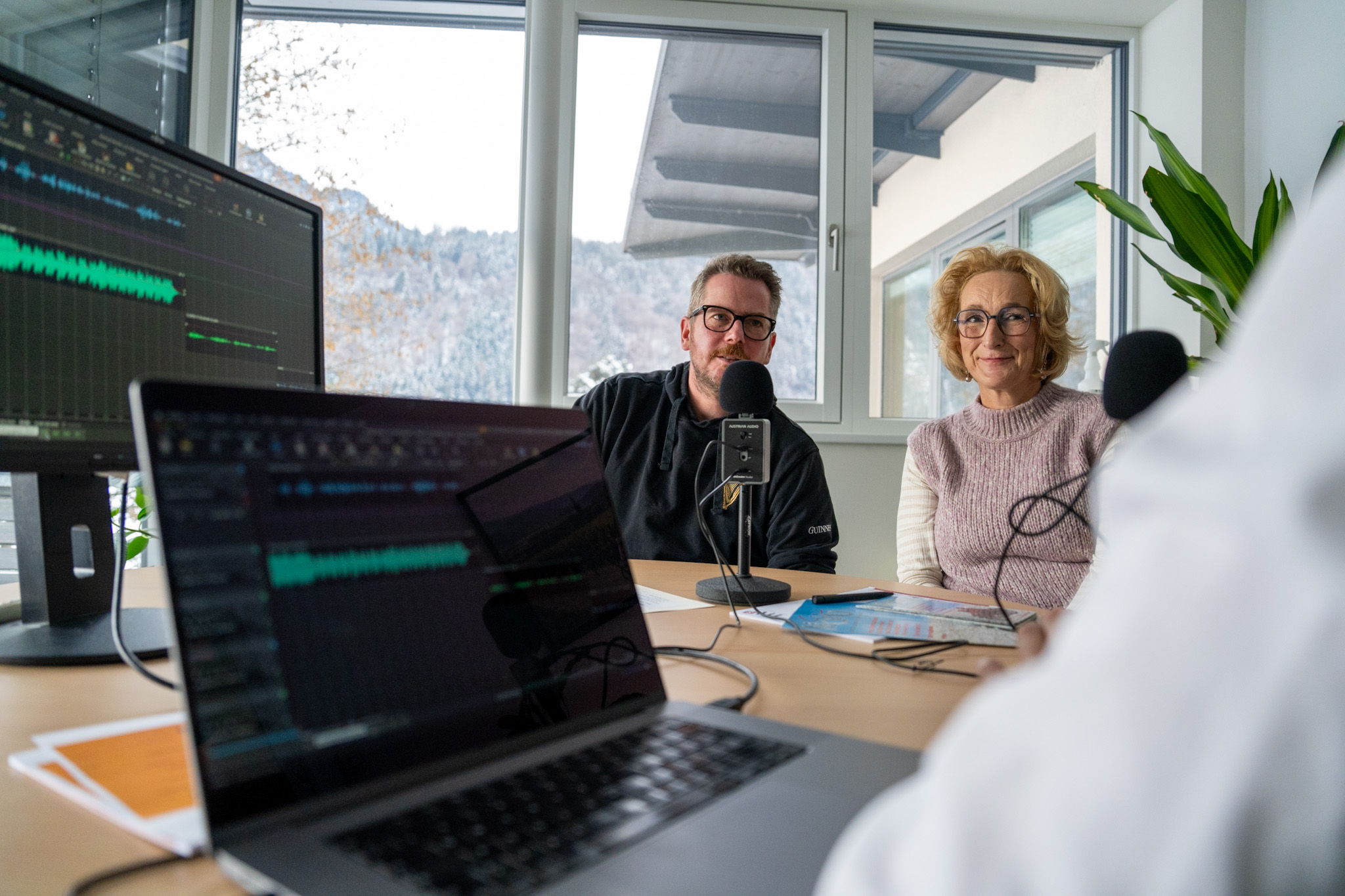 Zwei Personen in einem Podcast-Studio mit Mikrofonen und Audioaufnahmegerät
