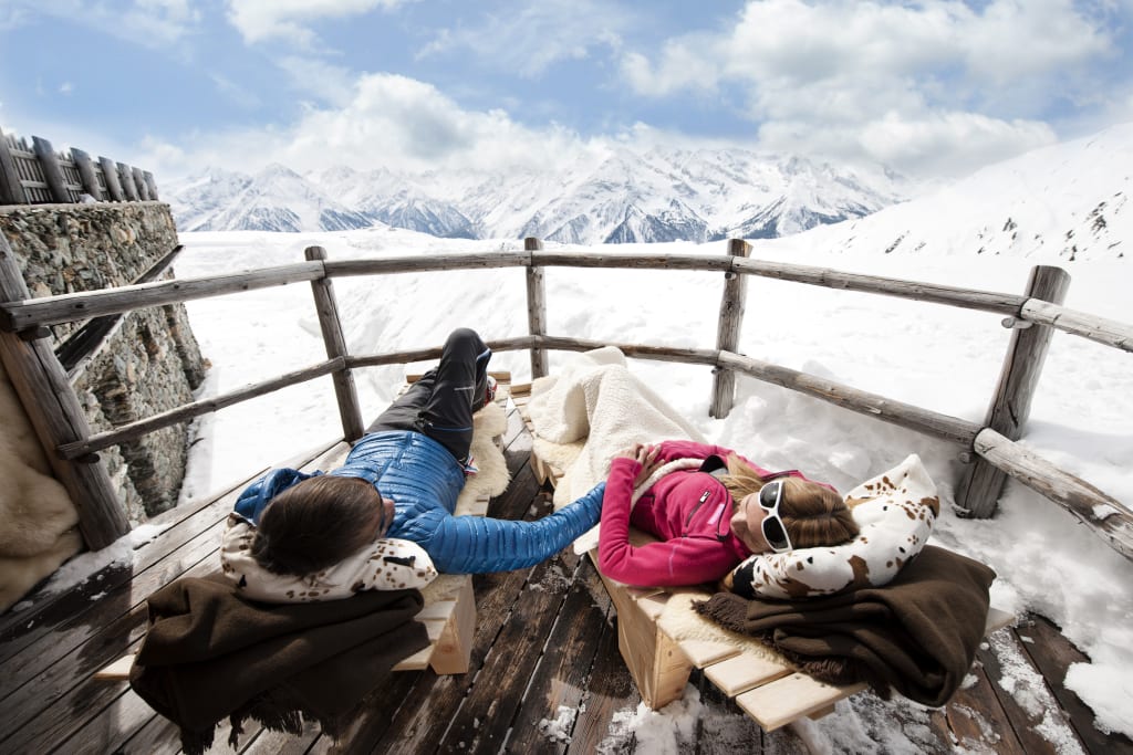 Zwei Personen entspannen auf einer Holzterrasse mit Blick auf verschneite Berge