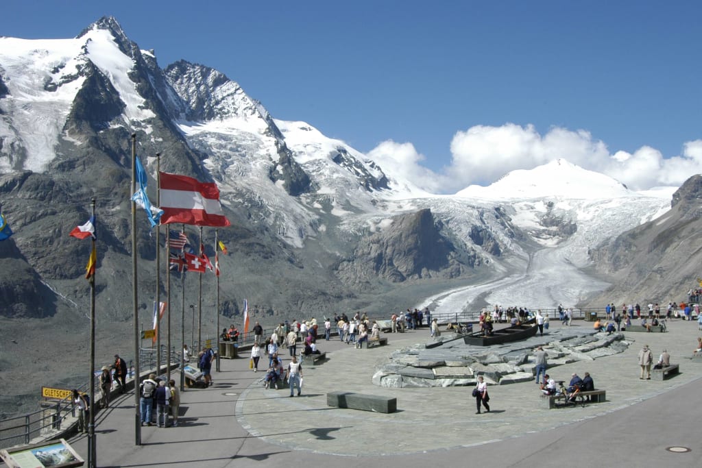 Besucher am Gletscher mit Bergpanorama und Fahnen im Hintergrund