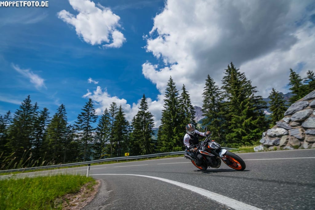 Motorradfahrer fährt um eine Kurve auf Bergstraße bei sonnigem Himmel