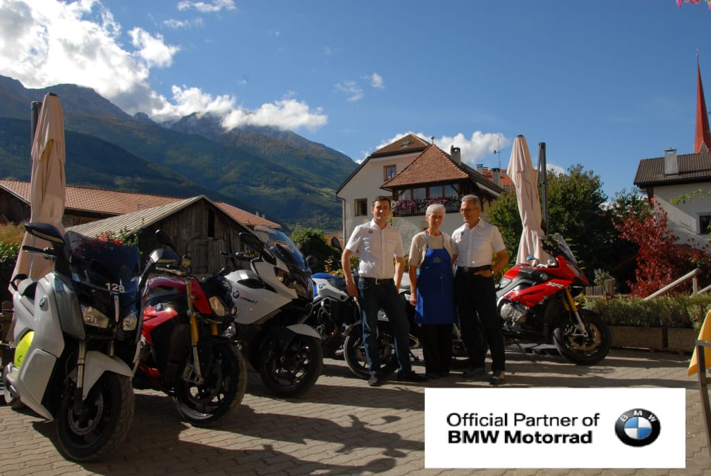 Drei Personen stehen vor mehreren BMW Motorrädern in einer Berglandschaft