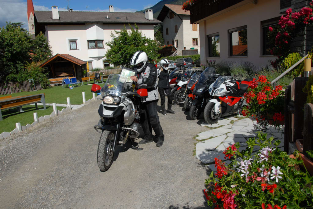 Motorradfahrer lesen Karten neben mehreren geparkten Motorrädern vor Häusern