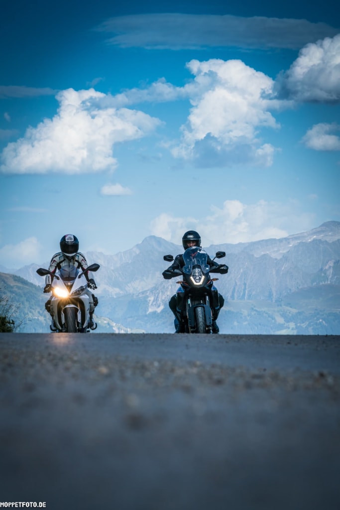 Zwei Motorradfahrer auf Bergstraße vor bewölktem Himmel